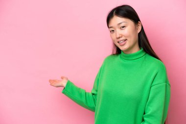 Young Chinese woman isolated on pink background extending hands to the side for inviting to come