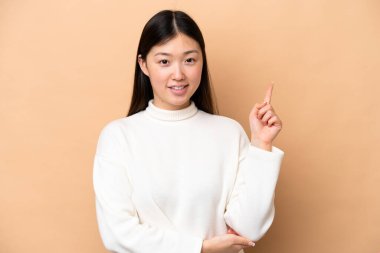 Young Chinese woman isolated on beige background happy and pointing up
