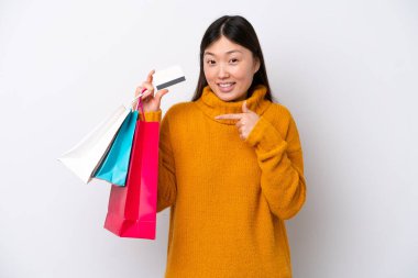 Beyaz arka planda izole edilmiş genç bir Çinli kadın elinde alışveriş çantaları ve bir kredi kartı tutuyor.