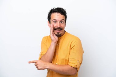 Young man with moustache isolated on white background pointing to the side to present a product and whispering something