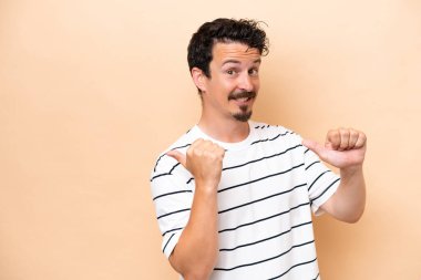 Beyazların arka planında izole edilmiş genç beyaz bir adam bir ürün sunmak için kenarı işaret ediyor.