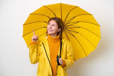 Yağmura dayanıklı ceketi ve şemsiyesi olan genç İngiliz kadın beyaz arka planda izole edilmiş harika bir fikre işaret ediyor.