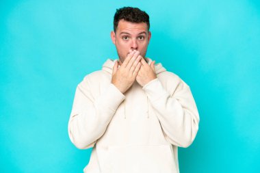 Beyaz tenli yakışıklı adam mavi arka planda izole edilmiş, ağzı elleriyle kapatıyor.