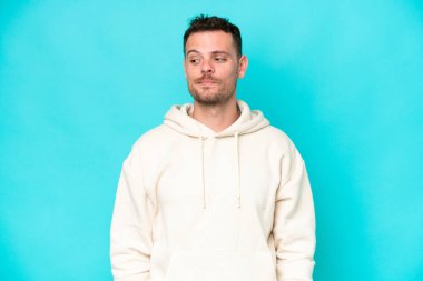 Mavi arka planda soyutlanmış beyaz, yakışıklı genç bir adam şüpheli hareketler yapıyor.