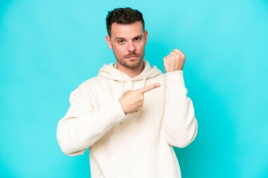 Beyaz tenli yakışıklı adam mavi arka planda izole edilmiş, geç kalma jesti yapıyor.