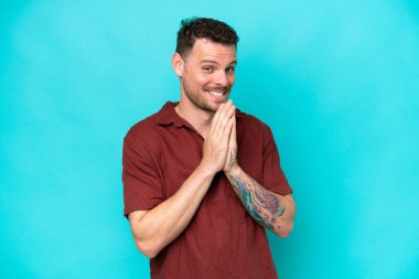 Mavi arka planda izole edilmiş beyaz tenli yakışıklı adam avuç içlerini bir arada tutuyor. İnsan bir şey ister.