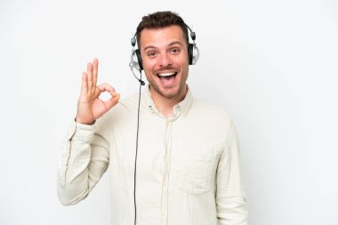 Tele pazarlamacı beyaz arka planda izole edilmiş bir kulaklıkla çalışan beyaz bir adam parmaklarıyla tamam işareti gösteriyor.