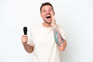 Young caucasian singer man picking up a microphone isolated on white background shouting with mouth wide open