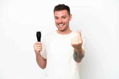 Young caucasian singer man picking up a microphone isolated on white background making money gesture