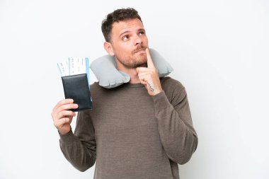 Young caucasian man holding a passport isolated on white background having doubts while looking up