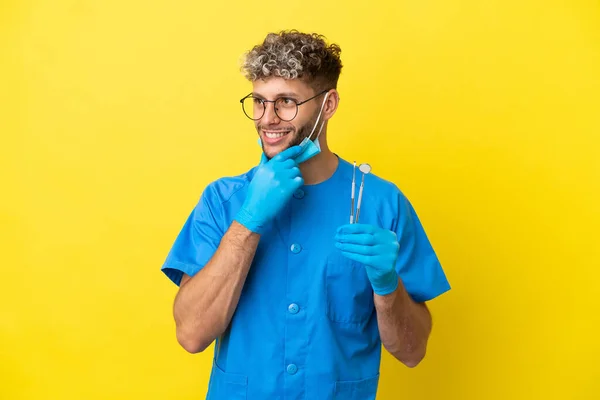 Dentista Caucasiano Homem Segurando Ferramentas Isoladas Fundo Amarelo Olhando Para — Fotografia de Stock