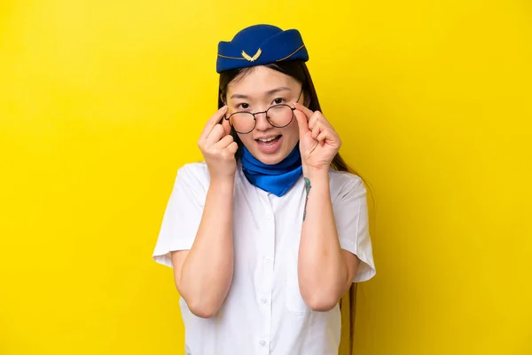 Airplane Chinese woman stewardess isolated on yellow background with glasses and surprised