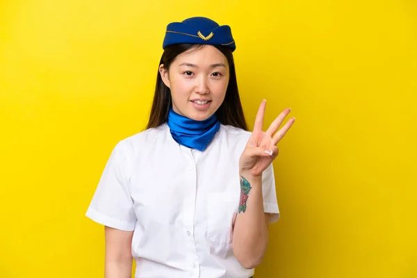 Airplane Chinese woman stewardess isolated on yellow background happy and counting three with fingers