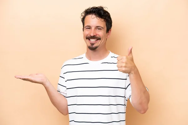 Young Caucasian Man Isolated Beige Background Holding Copyspace Imaginary Palm — Stock Fotó