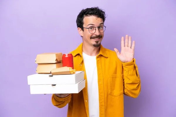 Young Caucasian Man Holding Fast Food Isolated Purple Background Saluting – stockfoto