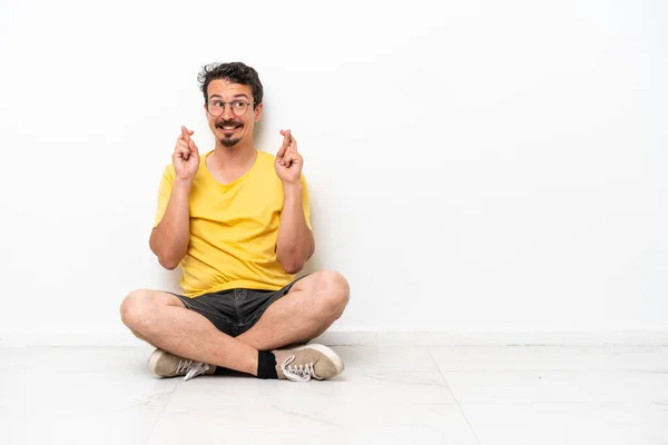 Young Caucasian Man Sitting Floor Isolated White Background Fingers Crossing — Foto de Stock