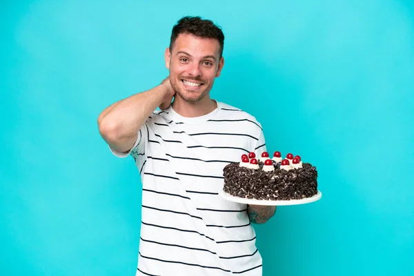Young caucasian man holding birthday cake isolated on blue background laughing