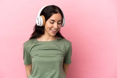 Pembe arka planda izole edilmiş beyaz bir kadın müzik dinliyor.