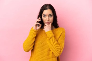 Young caucasian woman using mobile phone isolated on pink background thinking