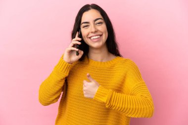 Young caucasian woman using mobile phone isolated on pink background giving a thumbs up gesture