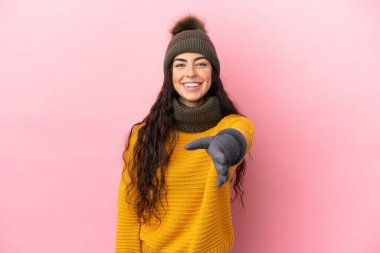Young caucasian girl with winter hat isolated on purple background shaking hands for closing a good deal