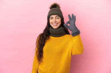 Young caucasian girl with winter hat isolated on purple background showing ok sign with fingers