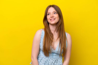 Kafkasyalı genç bir kadın sarı arka planda izole edilmiş bir şekilde yukarı bakarken bir fikir düşünüyor.