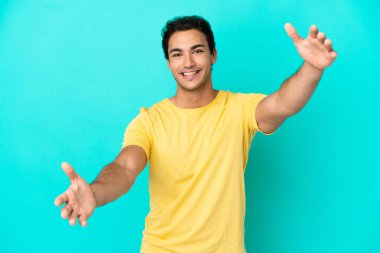 İzole edilmiş mavi arka planda beyaz yakışıklı bir adam sunar ve davet eder.