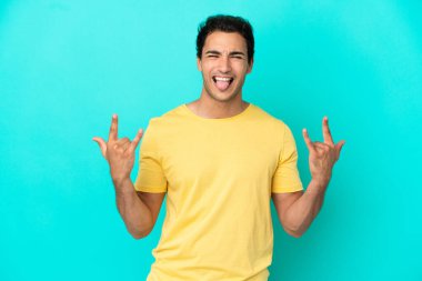 Caucasian handsome man over isolated blue background making horn gesture