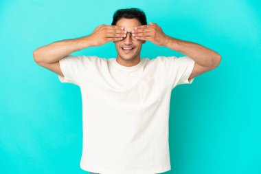 Caucasian handsome man over isolated blue background covering eyes by hands and smiling