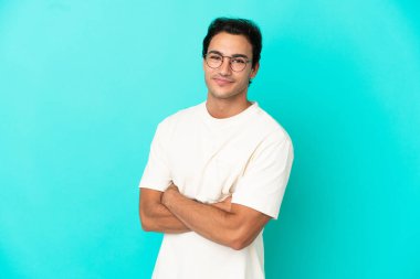 İzole edilmiş mavi arka planda kolları bağlı ve ileriye bakan beyaz yakışıklı bir adam.