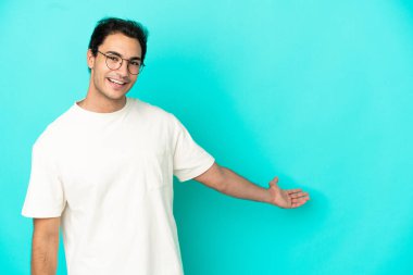 Izole mavi arka plan üzerinde Kafkas yakışıklı adam gelmeye davet için elleri yana uzatan