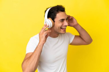 Caucasian handsome man over isolated yellow background listening music and singing