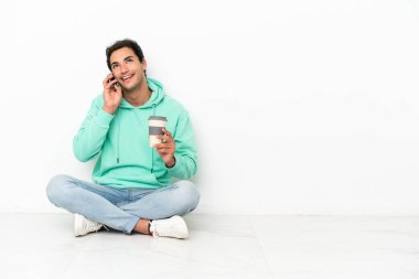 Kafkasyalı yakışıklı bir adam kahve alıp götürmek için yerde oturuyor ve bir de cep telefonu.