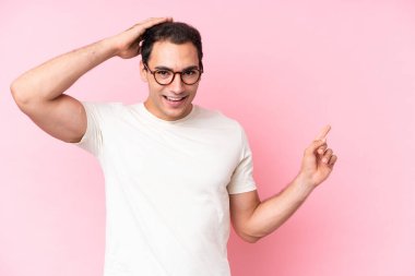 Pembe arka planda izole edilmiş genç beyaz adam şaşırmış ve parmağıyla kenarı işaret ediyor.