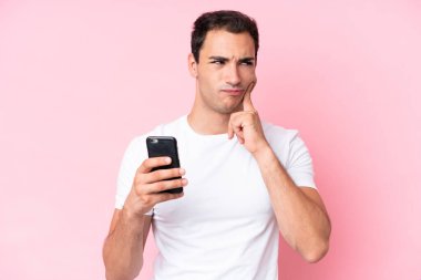 Young caucasian man isolated on pink background using mobile phone and thinking