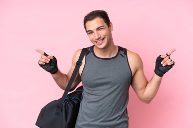 Young sport caucasian man with sport bag isolated on pink background pointing finger to the laterals and happy