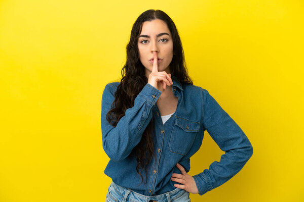 Young caucasian woman isolated on yellow background showing a sign of silence gesture putting finger in mouth