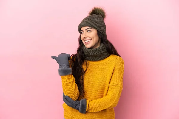 年轻的高加索女孩 头戴紫色背景的冬帽 指着侧面展示自己的产品 — 图库照片