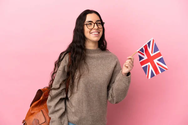 Young caucasian woman holding an United Kingdom flag isolated on pink background thinking an idea while looking up