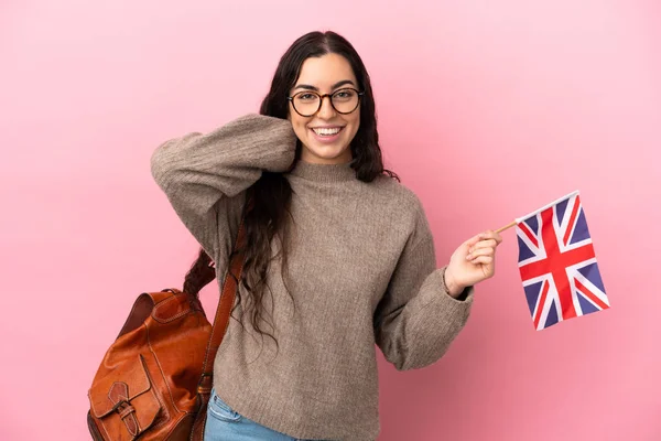 Young caucasian woman holding an United Kingdom flag isolated on pink background laughing