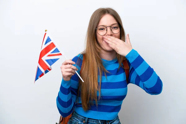 Young caucasian woman holding an United Kingdom flag isolated on white background happy and smiling covering mouth with hand