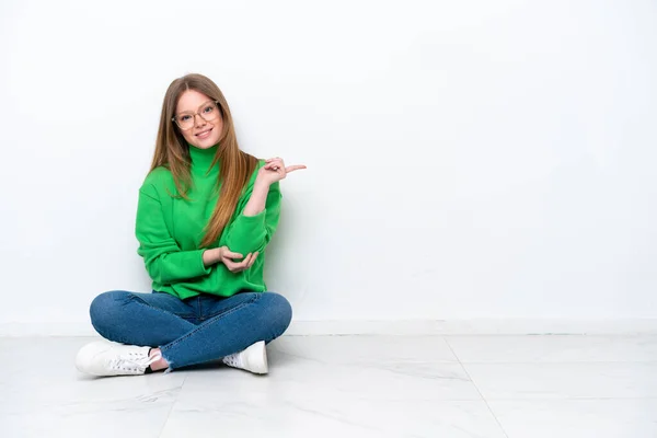 若い白人女性の床の上に白い背景に指を指す上に座っ側面 — ストック写真