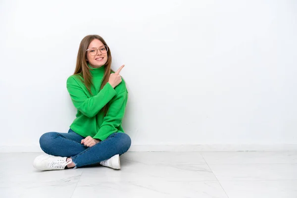 Mladé Běloška Žena Sedí Podlaze Izolované Bílém Pozadí Ukazuje Straně — Stock fotografie