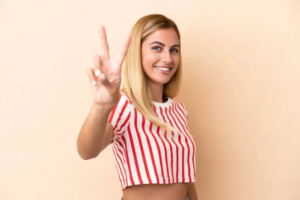 Blonde Uruguayische Mädchen Isoliert Auf Beigem Hintergrund Lächelnd Und Zeigt — Stockfoto