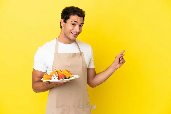 Restaurant Waiter Holding Waffles Isolated Yellow Background Pointing Finger Side — Fotografia de Stock