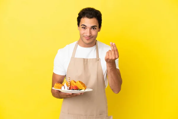 Restaurant Waiter Holding Waffles Isolated Yellow Background Making Money Gesture — Zdjęcie stockowe
