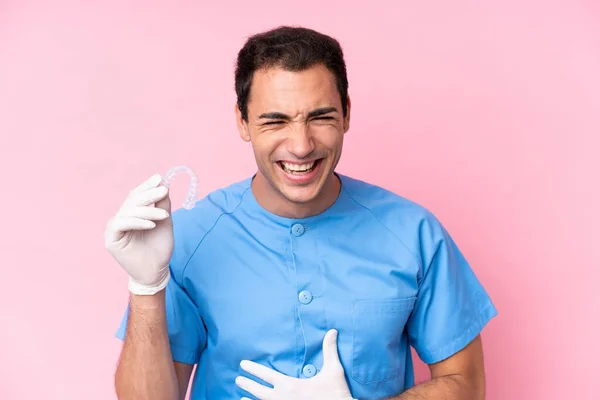 Dentist caucasian man holding invisible braces isolated on pink background smiling a lot