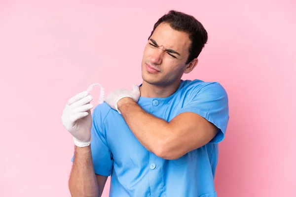 Dentist caucasian man holding invisible braces isolated on pink background suffering from pain in shoulder for having made an effort