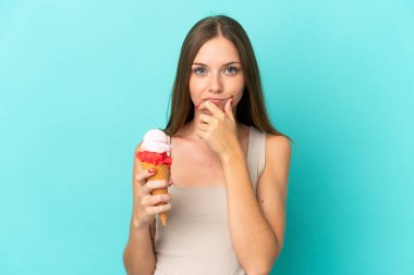 Kornet dondurmalı genç Litvanyalı kadın mavi arka planda izole edilmiş olarak düşünüyor.